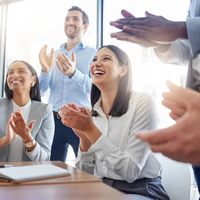 Diverse business team applauding during a meeting in a bright modern office with notebooks on the table