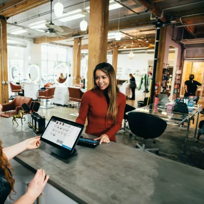 Customer paying at a modern hair salon reception with a smiling receptionist and digital payment system.