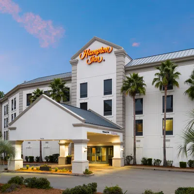 Exterior view of Hampton Inn hotel with palm trees at dusk under a blue and pink sky.