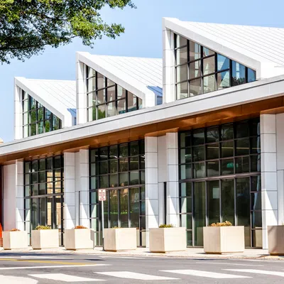 Modern building with large glass windows, white angled roofs, and planters lining the sidewalk under a sunny sky