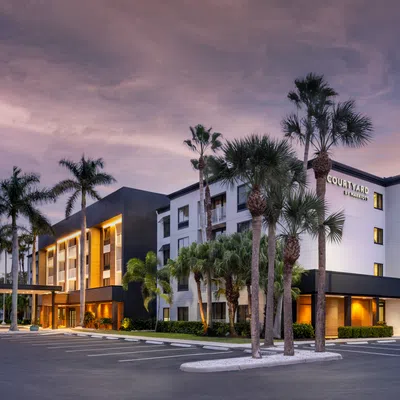 Modern Courtyard by Marriott hotel building with palm trees under a dramatic evening sky in a spacious parking lot.