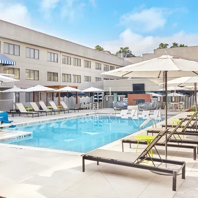 Bright outdoor hotel pool area with lounge chairs, umbrellas, and clear blue water on a sunny day