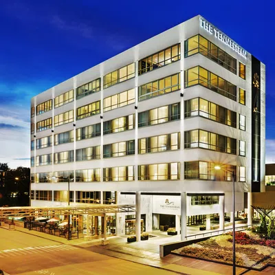 Modern six-story building of The Tennessean hotel illuminated at dusk with outdoor seating area and landscaped surroundings.