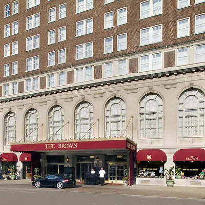 Front view of The Brown hotel with red awnings and people standing at the entrance on a sunny day.