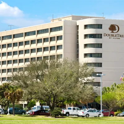 Exterior view of DoubleTree by Hilton hotel building with trees and parked cars under a blue sky.