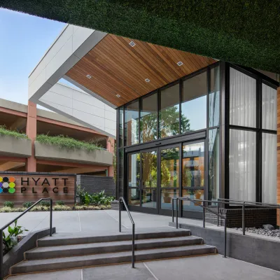 Entrance of Hyatt Place hotel with modern architecture, wooden accents, glass doors, and greenery.
