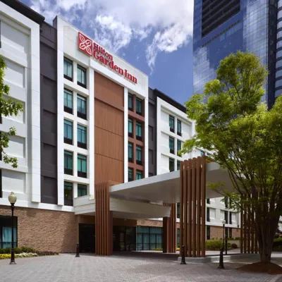 Hilton Garden Inn hotel exterior with modern facade, glass windows, trees, and a covered entrance under a blue sky.