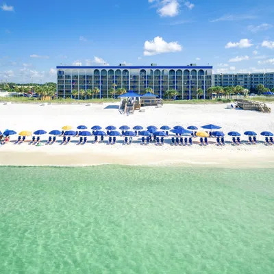 Clear turquoise ocean water with sandy beach and rows of blue and yellow umbrellas in front of beachfront resort.