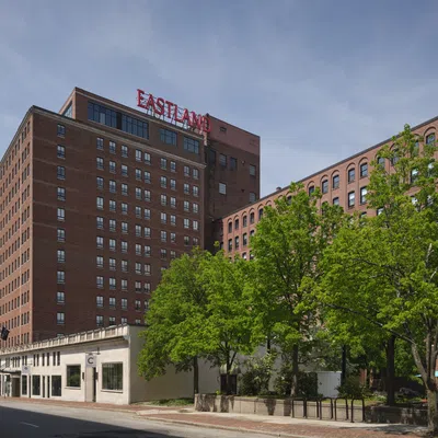 Large brick building with Eastland sign at the top and green trees in front under a cloudy sky.