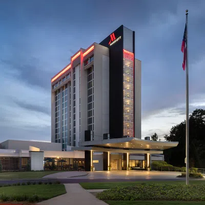 Marriott hotel building at dusk with illuminated signage and flags outside under a cloudy sky.