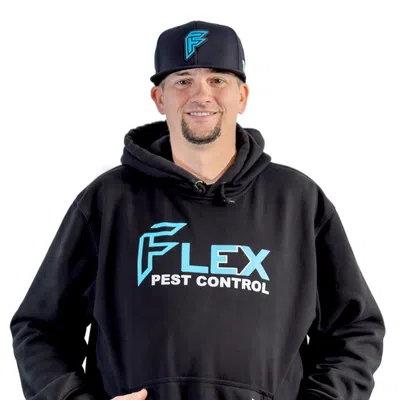 Man wearing black Flex Pest Control hoodie and cap smiling with hands in hoodie pocket on white background