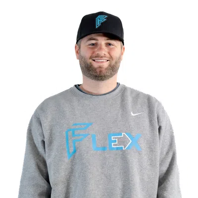 Smiling man wearing a gray Flex sweatshirt and black cap with logo, hands in pockets, standing against white background.
