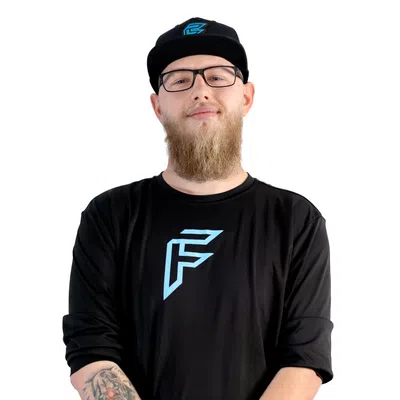 Bearded man with glasses and tattoo wearing black shirt and cap with blue logo on white background