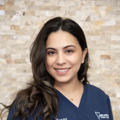 Smiling female dentist with long dark hair wearing navy scrubs labeled Dr. Hanna in a warm office setting.