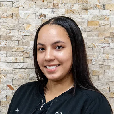 Smiling woman in black dental scrubs with Midland Park Family Dentistry logo against stone wall background
