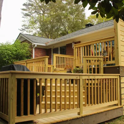 Newly built wooden deck with railings and stairs attached to a suburban brick house surrounded by trees.