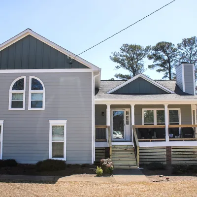 Gray two-story house with white trim, front porch, and multiple windows under a clear blue sky.