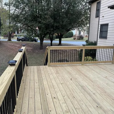 New wooden backyard deck with black metal railing attached to beige house, surrounded by trees and grass.