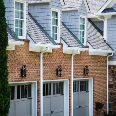Row of three gray garage doors with brick facade, dormer windows, and exterior lantern lights on a residential home