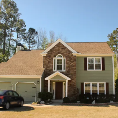 Inviting two-story home with stone accents, green siding, and well-maintained garden under a clear blue sky.