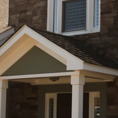 Front porch with white columns and gabled roof attached to brown stone and tan house exterior.