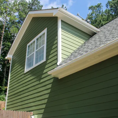 Green siding on modern house with white trim and window under clear blue sky with trees background