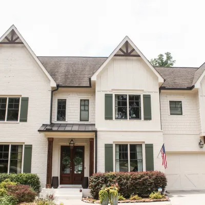 Two-story white suburban house with dark green shutters, a front porch, and an attached garage with American flag.