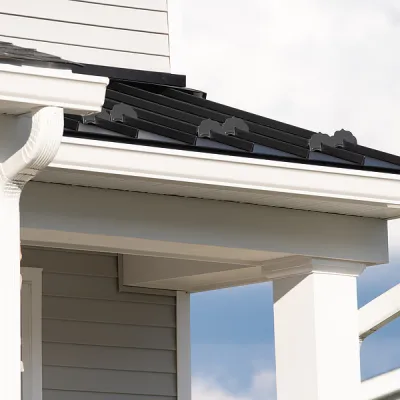 Close-up of a modern roof with stylish metal shingles and white gutters under a blue sky.