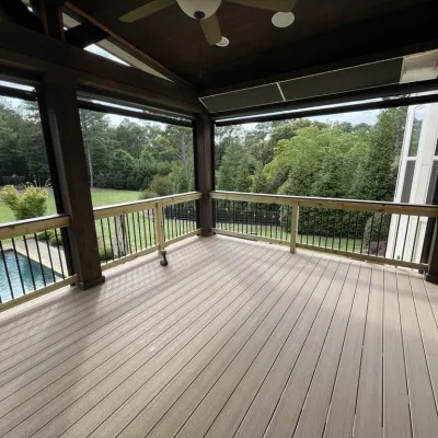 Spacious covered deck with wooden flooring and railing overlooking a pool and green backyard landscape.