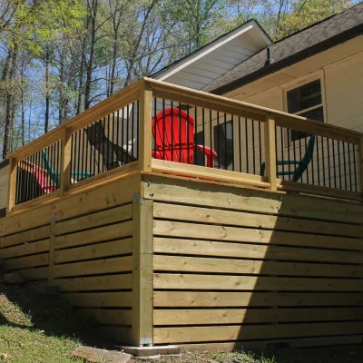 Elevated wooden deck attached to a white house with colorful outdoor chairs and surrounding trees in spring.