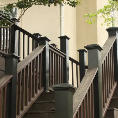 Brown wooden outdoor staircase with black railings surrounded by trees against beige building