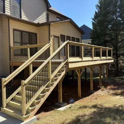 Elevated wooden deck with stairs and metal railings attached to a beige two-story house with backyard trees.