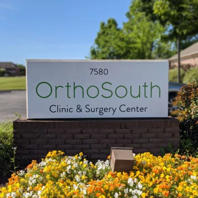 OrthoSouth Clinic & Surgery Center sign with flowers and greenery in a sunny outdoor setting.