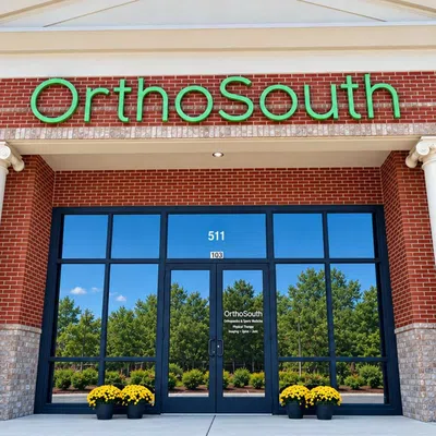 OrthoSouth medical office entrance with glass doors, red brick facade, white columns, and green signage.