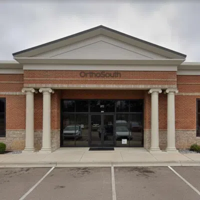 Exterior view of a brick commercial building with columns and glass entrance under a cloudy sky.