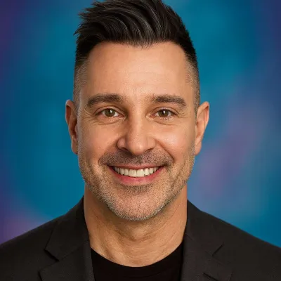 Smiling man with dark hair wearing a black blazer against a blue and purple gradient background.