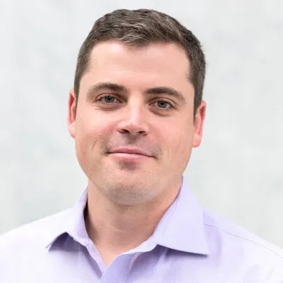 Portrait of a smiling man wearing a light purple dress shirt against a plain light gray background