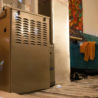 Indoor home furnace unit in a cozy living room with a sofa, rug, and drum set beside it.