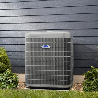 Outdoor Carrier air conditioning unit installed beside a house with bushes and stones around it