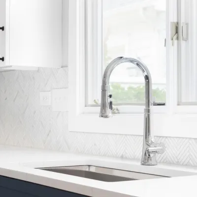 Modern kitchen with sleek chrome faucet by window, herringbone backsplash, and clean white surfaces.