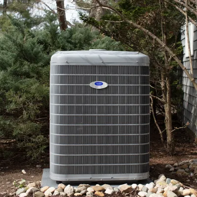 Outdoor Carrier Infinity gray air conditioning unit installed on concrete pad surrounded by rocks and trees.