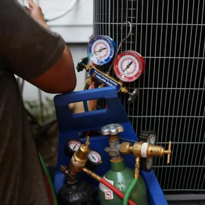 HVAC technician checking refrigerant pressure gauges connected to an air conditioning unit outdoors