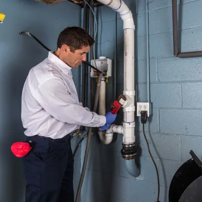 Plumber using a wrench to fix white PVC pipes against a blue wall in a utility room.