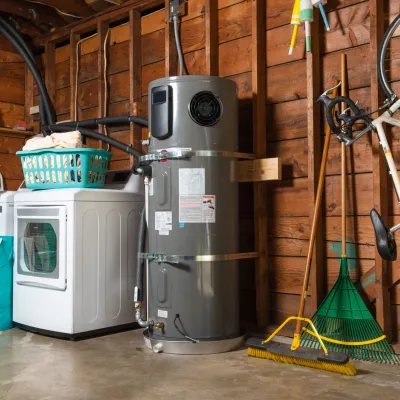 A functional garage with a water heater, washer, storage basket, and cleaning tools neatly arranged.
