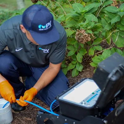 Technician in blue uniform and orange gloves working with fiber optic cables near a house garden.