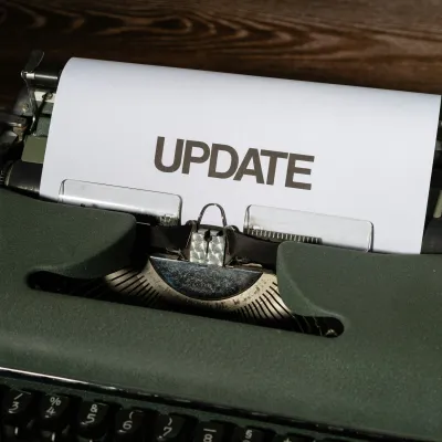 Vintage typewriter typing the word UPDATE on white paper on a wooden surface.