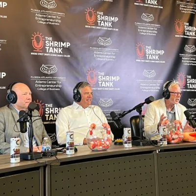 Three men wearing headphones speaking into microphones during The Shrimp Tank podcast recording session