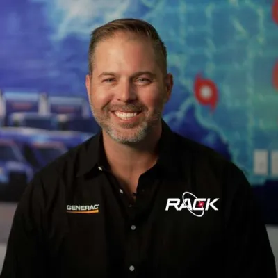 Smiling man in Generac branded shirt with RACK logo, trucks and mapped pins in the background.