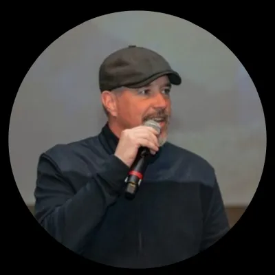 Man wearing a cap speaking into a microphone against a blurred background in a circular frame