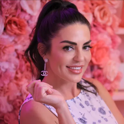 Smiling woman with dark hair in floral dress wearing dangling earrings against pink floral backdrop